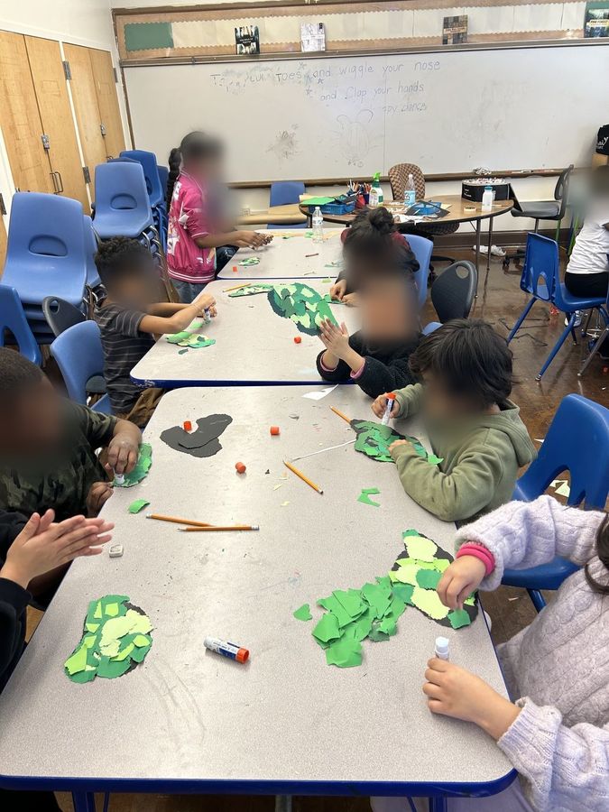 Children at long classroom tables working on a torn-paper art project