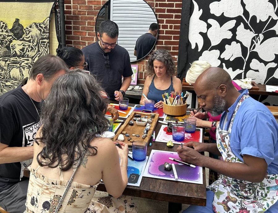 Adults gathered around a table painting rocks at a focus group session