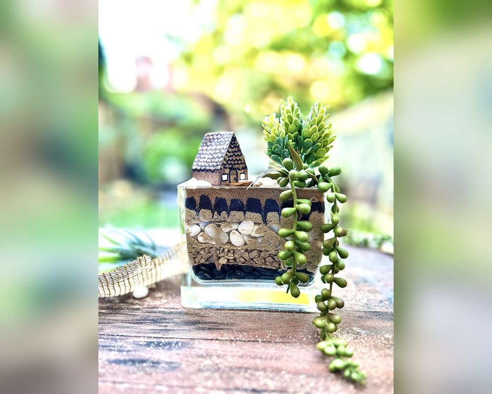A finished terrarium in a glass vase with a little house and a trailing succulent